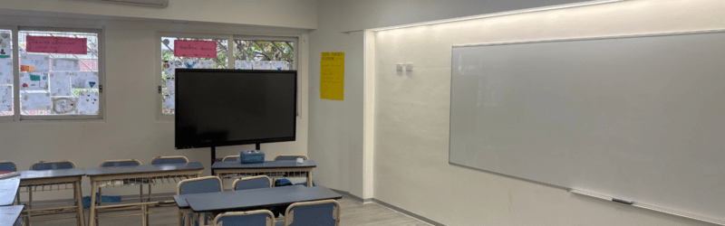 Detalle de aula con pantalla digital, pizarra blanca y paredes con acabados profesionales.